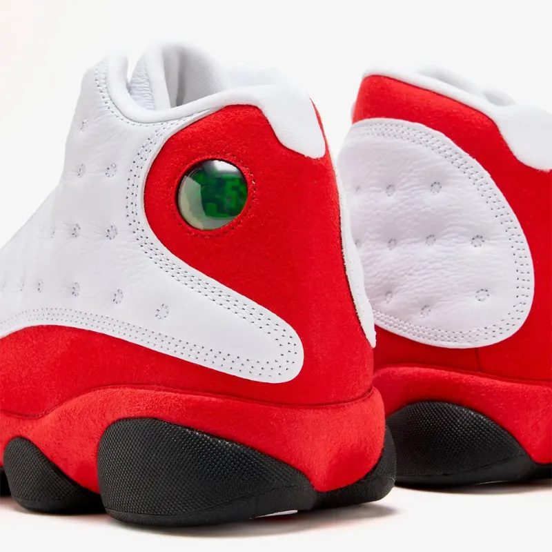 Close-up rear view of the Jordan 13 “Chicago/True Red” (2026), showing the red suede heel, white tumbled leather upper, and green holographic “cat eye” detail.